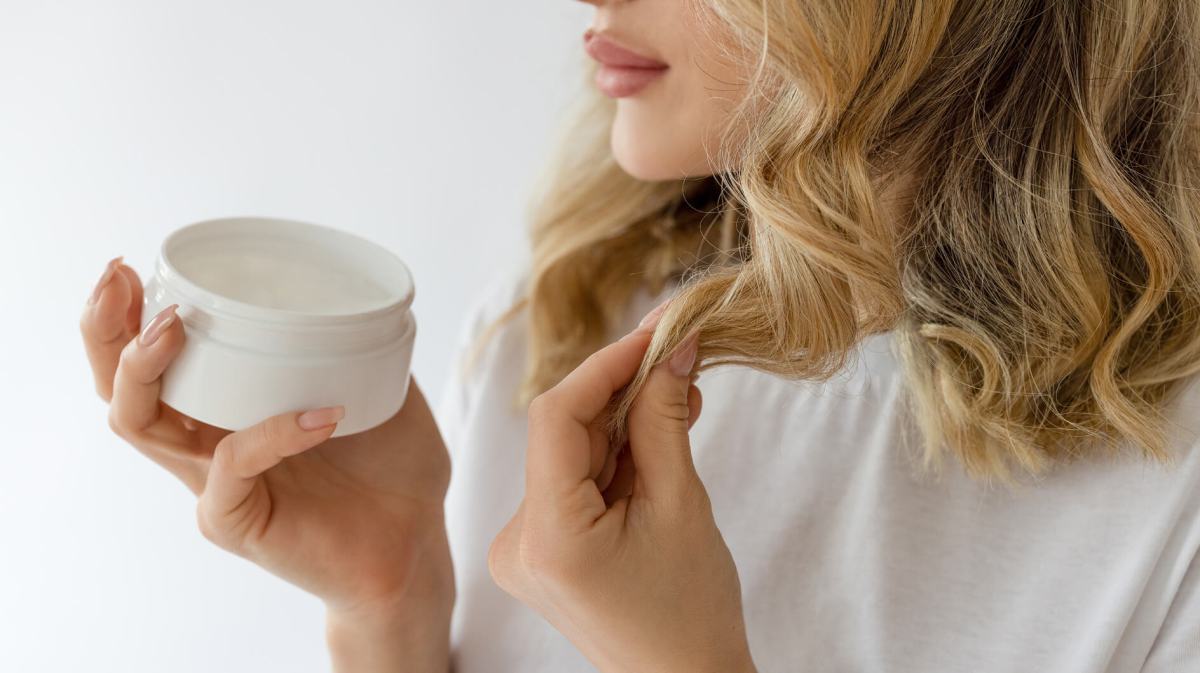 Frau mit blonden, kurzen Haaren gibt sich Haarkur in die Spitzen.