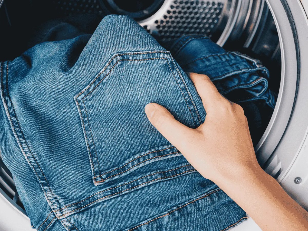 Person gibt Jeans in Waschmaschine.