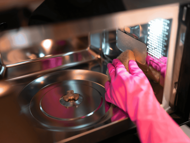 Person wischt Mikrowelle aus.