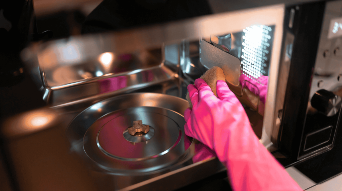 Person wischt Mikrowelle aus.