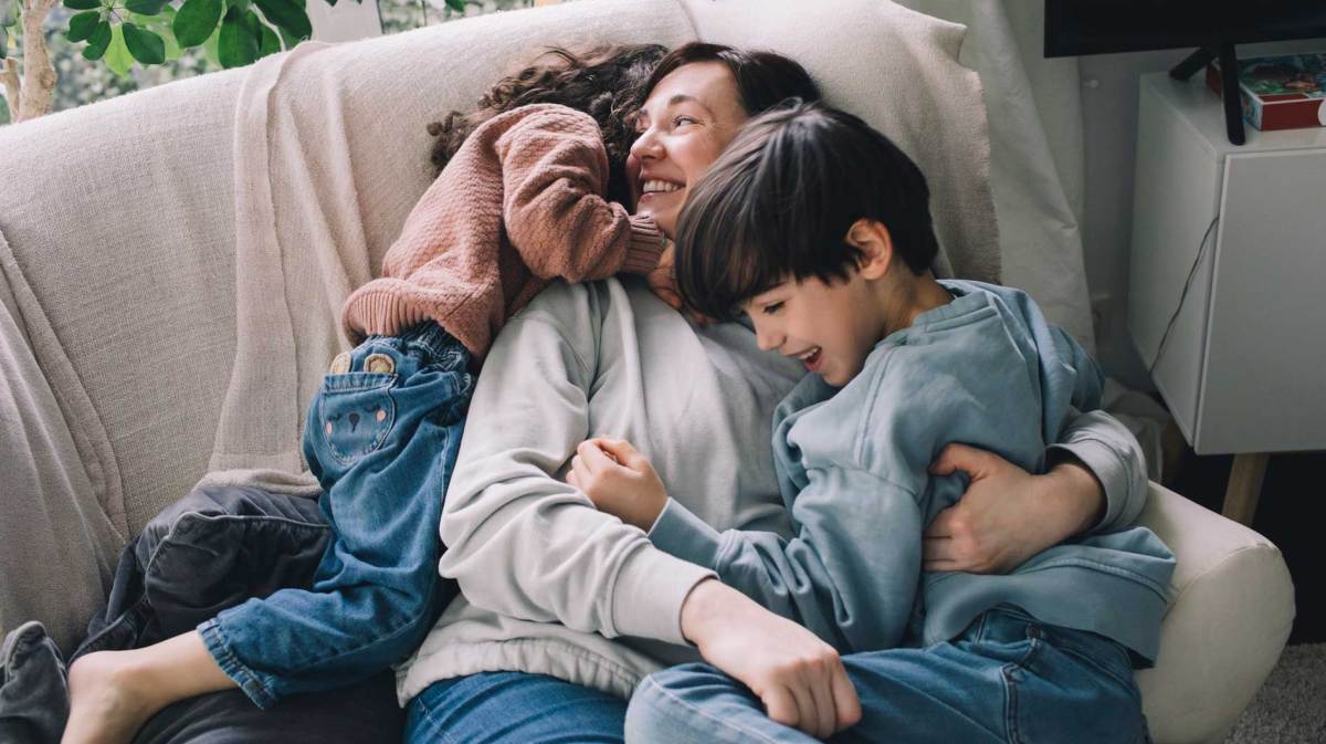 Mutter kuschelt mit ihren beiden Kindern auf dem Sofa.