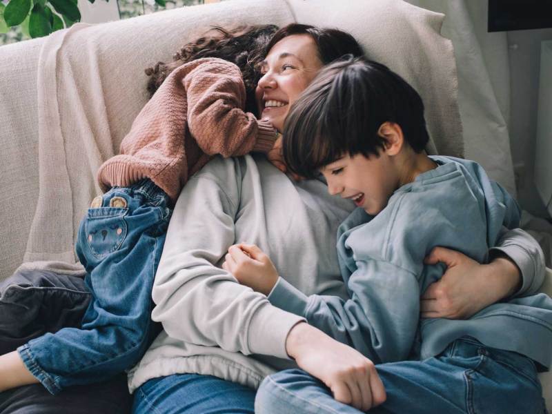 Mutter kuschelt mit ihren beiden Kindern auf dem Sofa.