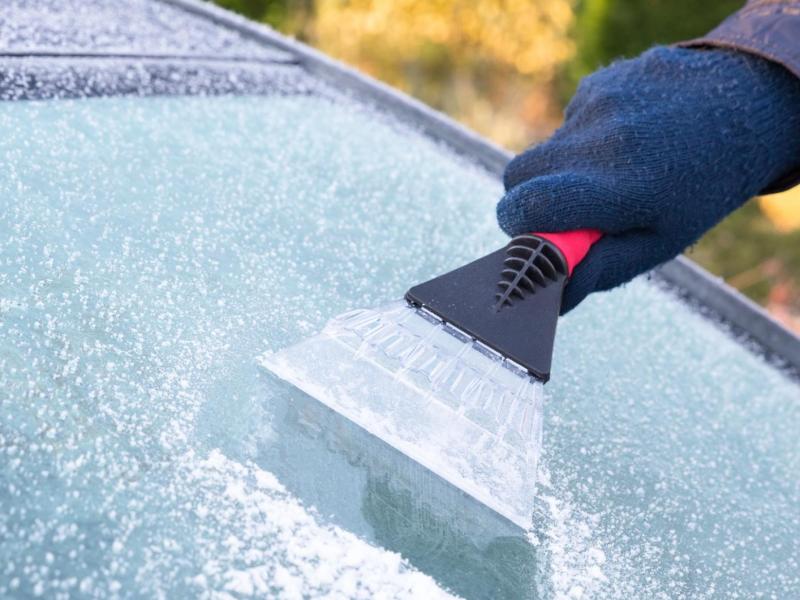 Person kratzt Eis von der Frontscheibe.