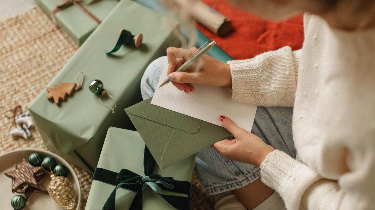 Frau schreibt umgeben von Geschenken auf ein Blatt Papier.