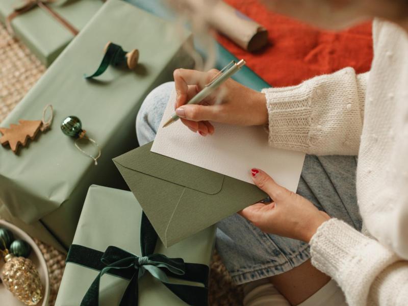 Frau schreibt umgeben von Geschenken auf ein Blatt Papier.