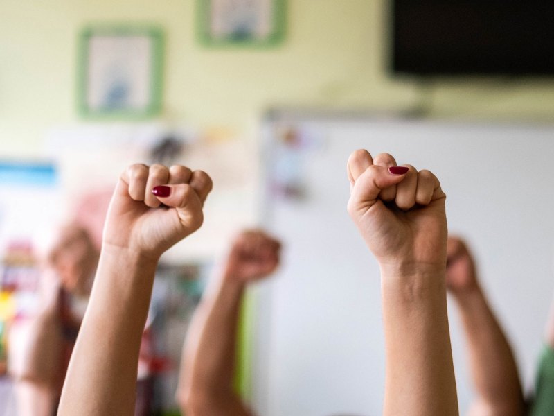 Hände zu Fäusten geballt werden in einem Klassenzimmer in die Höhe gestreckt.