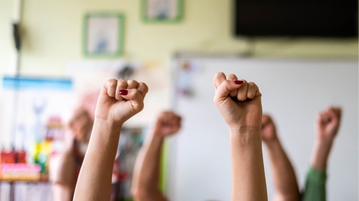 Hände zu Fäusten geballt werden in einem Klassenzimmer in die Höhe gestreckt.