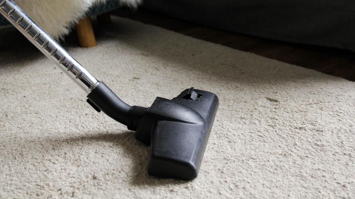 Ein Teppich wird mit einem Staubsauger abgesaugt.