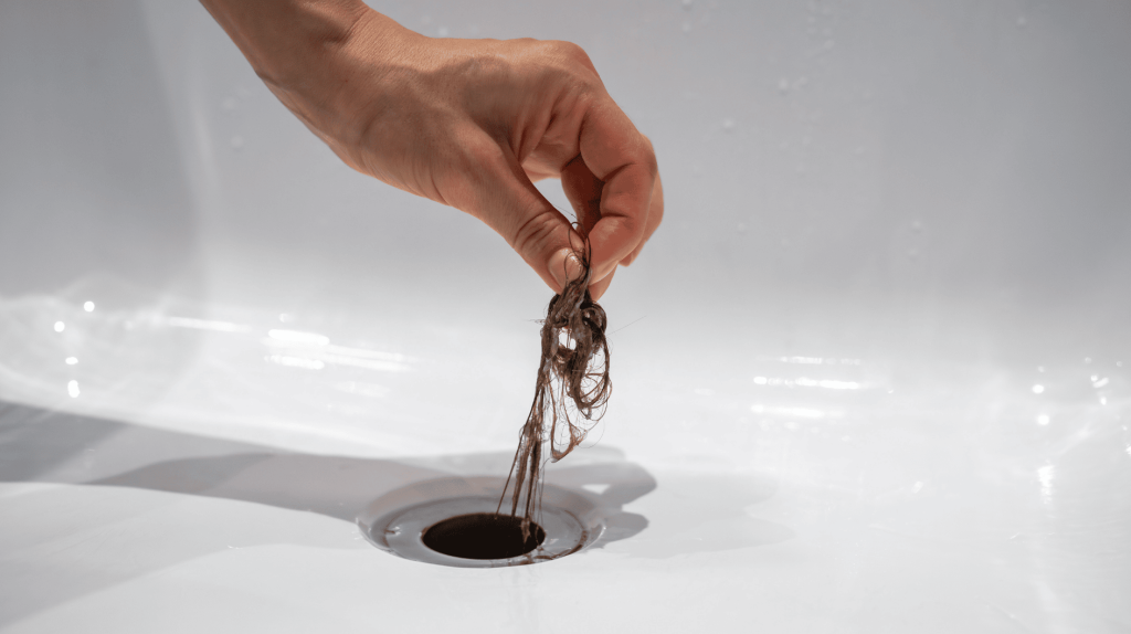 Person zieht Haarb&uuml;schel aus Abfluss.