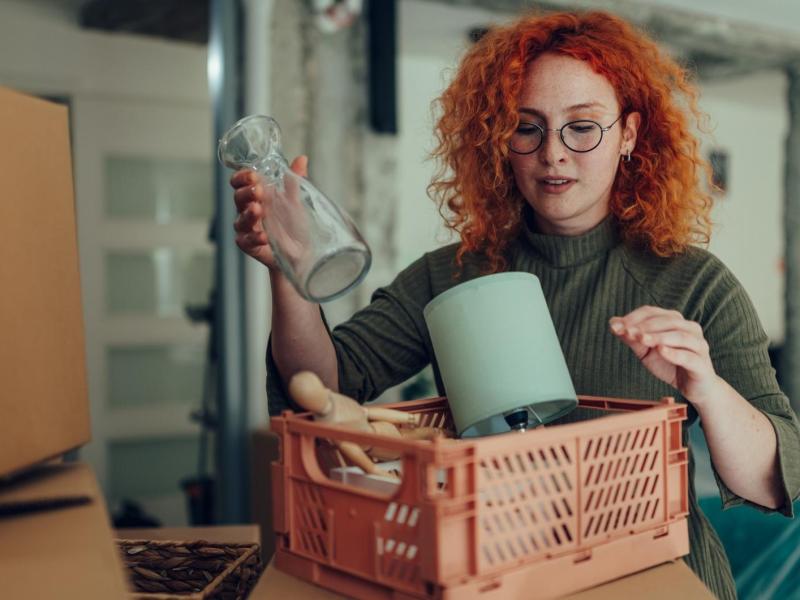 Rothaarige Frau r&auml;umt Gegenst&auml;nde in eine Kiste.
