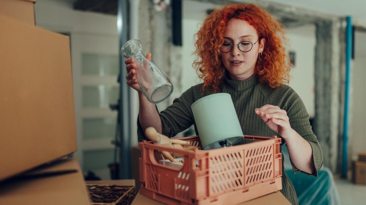 Rothaarige Frau räumt Gegenstände in eine Kiste.