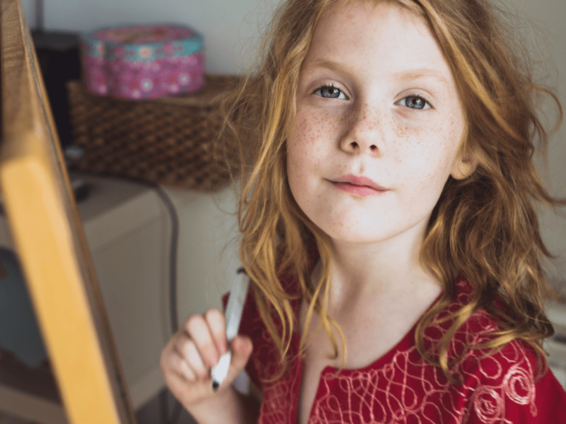 M&auml;dchen mit roten Haaren und einem Stift in der Hand schaut selbstbewusst