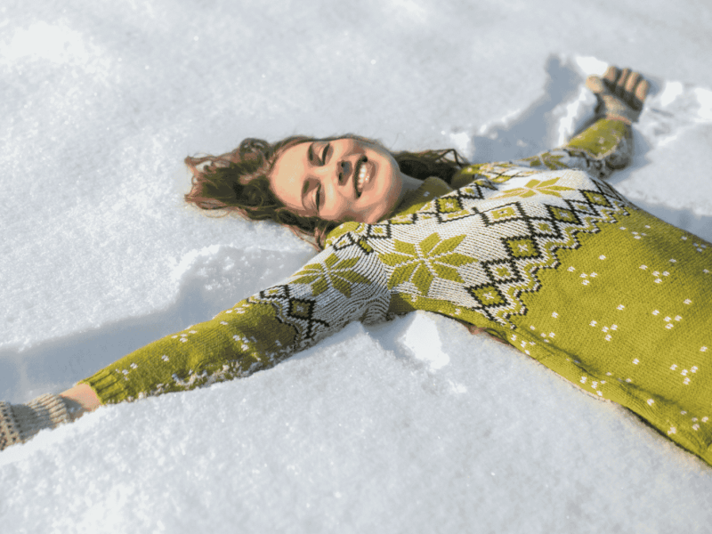 Frau in Wollpullover liegt im Schnee.