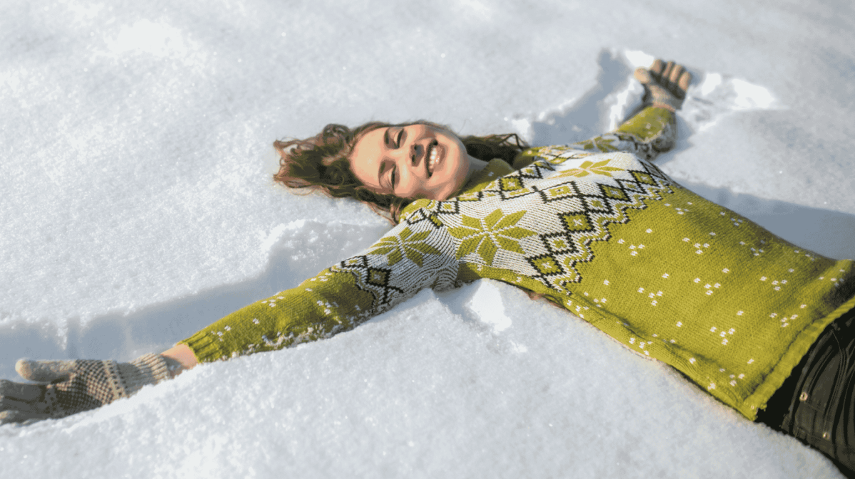Frau in Wollpullover liegt im Schnee.