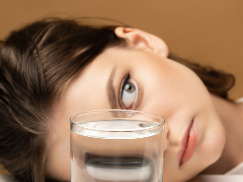 Frau liegt hinter einem Wasserglas, das ihre Gesichtszüge verzerrt
