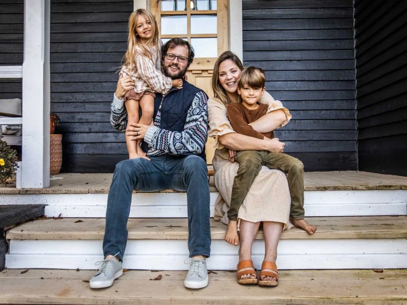 Mutter, Vater und zwei Kinder sitzen auf der Veranda ihres Hauses und posieren f&uuml;r ein Familienfoto.