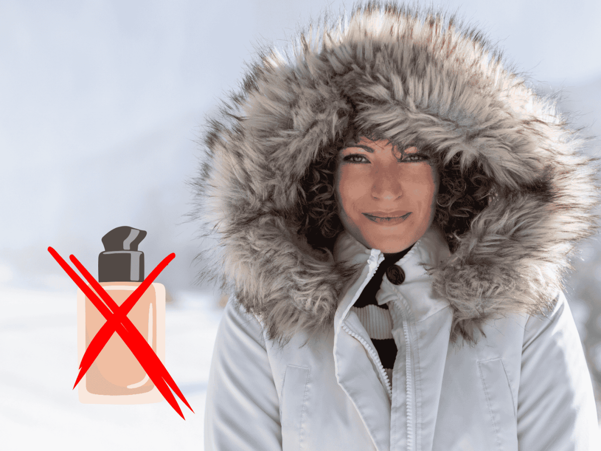 Junge Frau streht mit dicker Winterjacke und Kapuze auf dem Kopf in Schneelandschaft
