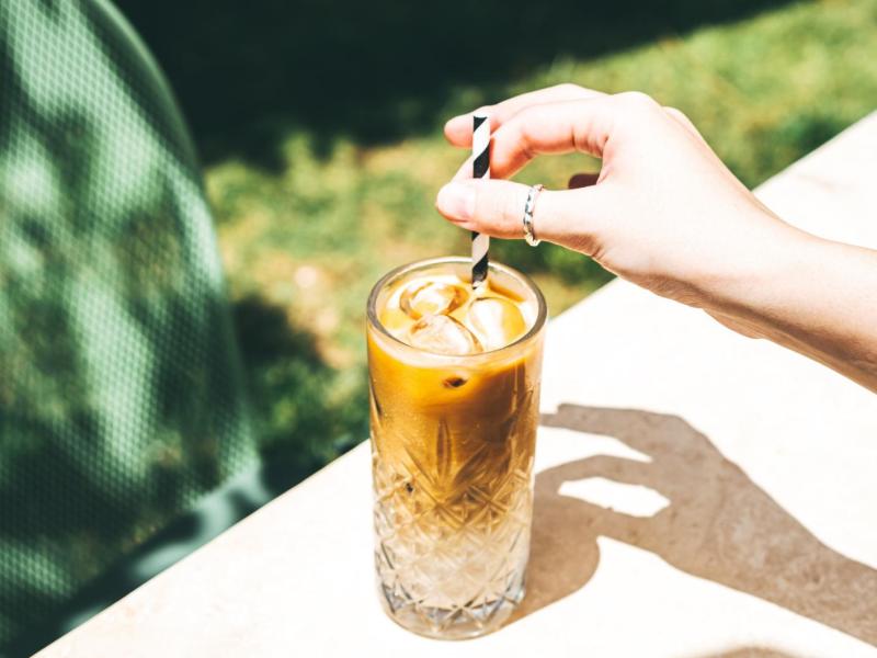 Frau rührt draußen in einem Glas mit Iced Coffee.