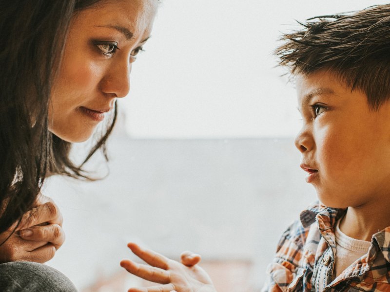 Mutter und Sohn sitzen sich nah bei einander gegenüber und der Sohn schaut seine Mutter bittend an.