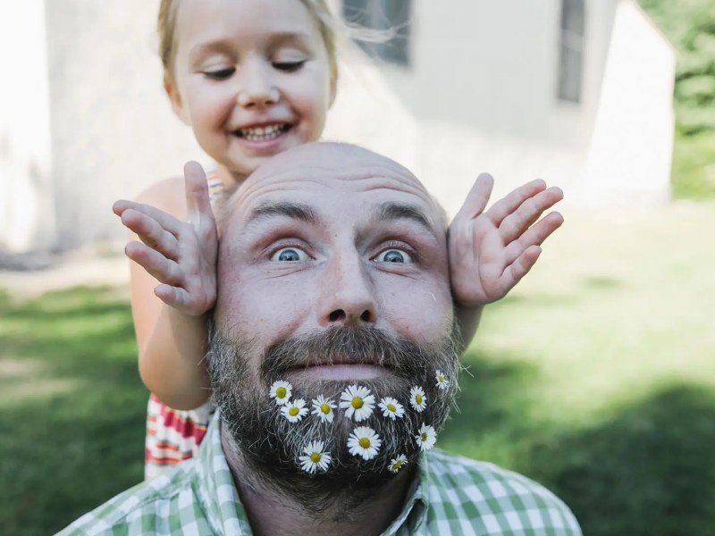 Nahaufnahme von Vater, mit Blumen im Bart und Tochter. Beide posieren f&uuml;r die Kamera.
