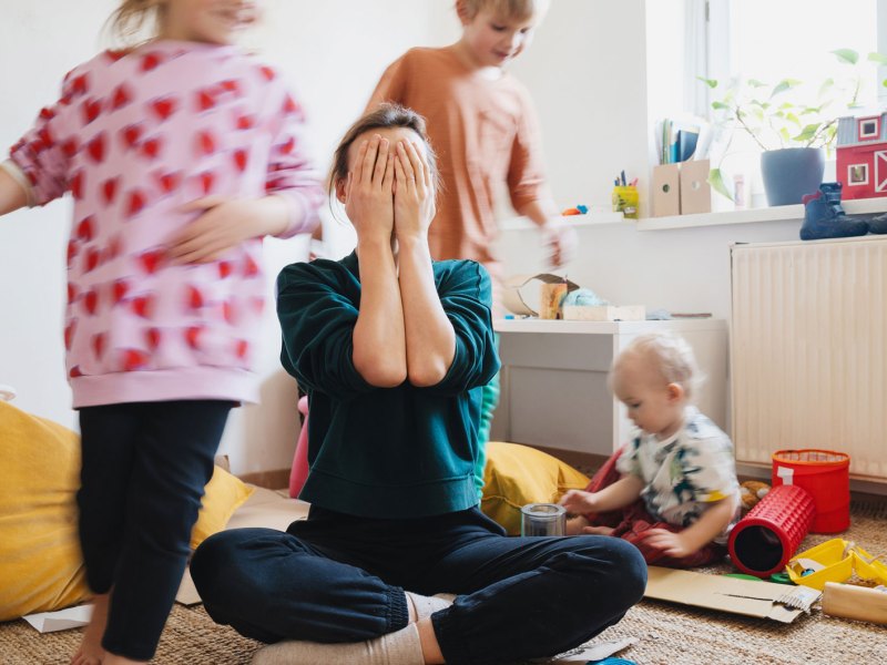 Mutter schlägt Hände vors Gesicht, Kinder toben wild um sie herum