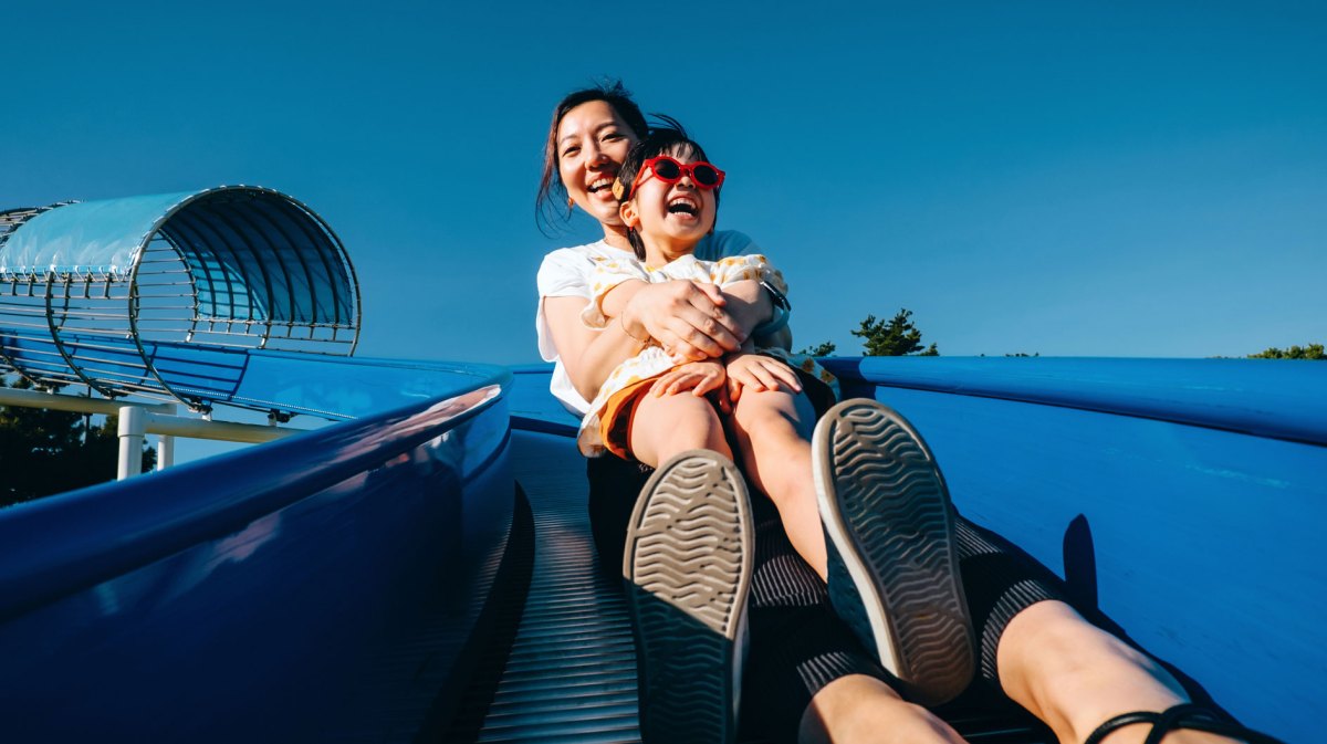Millenial Mama mit Tochter auf blauer Rutsche