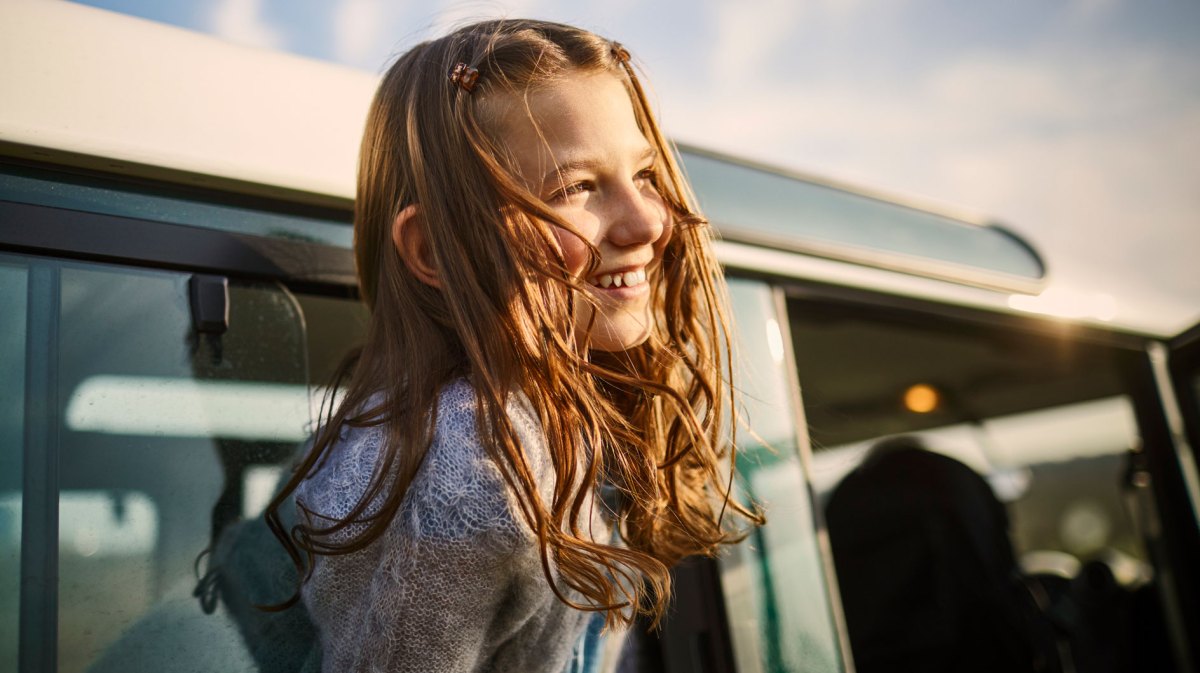 Mädchen schaut an einem schönen Sommerabend glücklich aus dem Fenster eines Autos.
