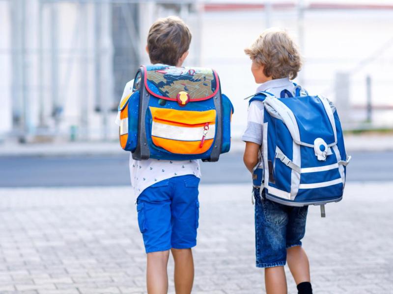 zwei Jungs mit Schulranzen gehen draußen gemeinsam.