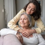 Junge Frau umarmt ihre ältere Mutter auf der couch.