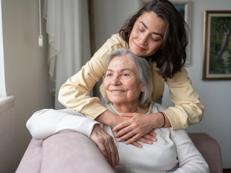 Junge Frau umarmt ihre &auml;ltere Mutter auf der couch.