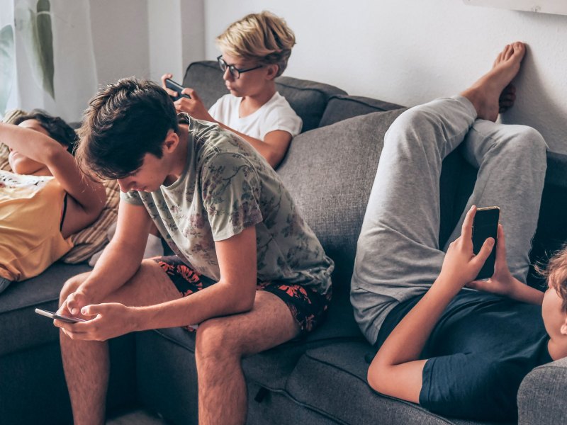Vier Teenager hängen auf dem Sofa ab, all mit dem Handy in der Hand.