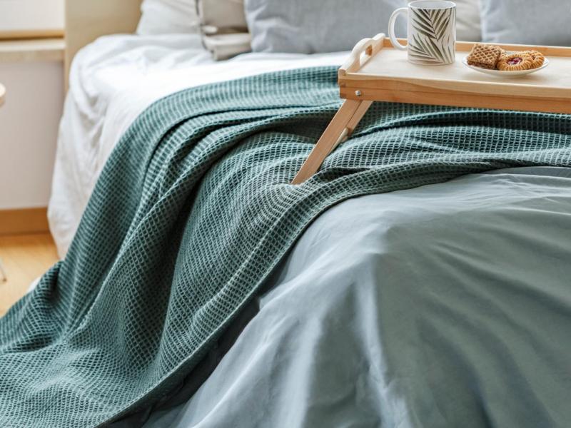 Auf einem Bett liegt eine grün-blaue Tagesdecke und darauf steht ein Tablett mit Tassen und Tellern drauf.
