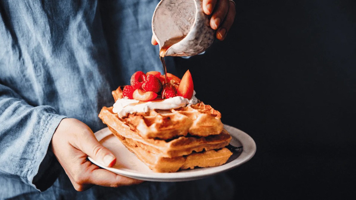 Frau gießt Sirup auf frische Waffeln mit Erdbeeren.