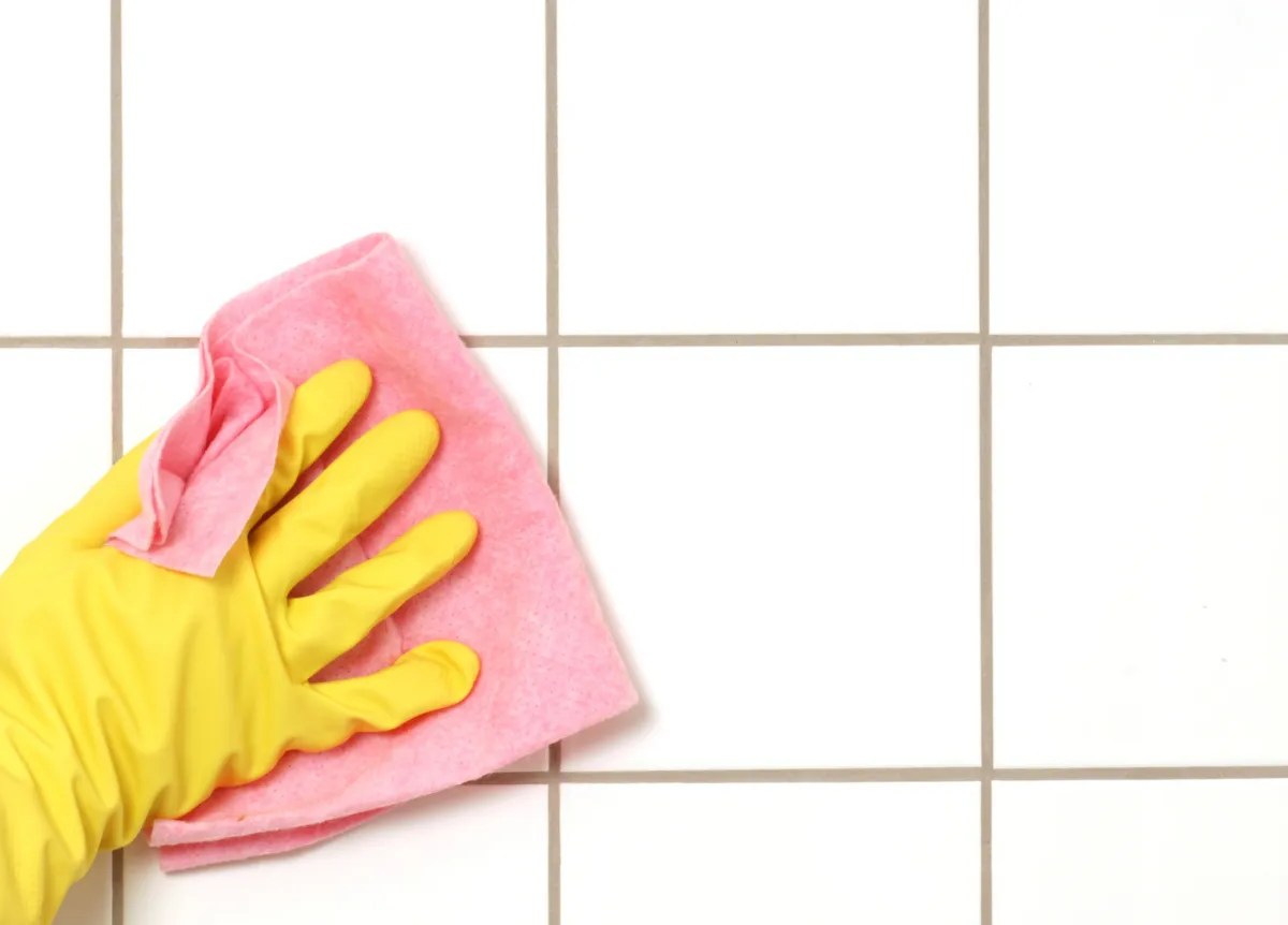 Person wischt mit rosa Lappen über Fugen in Badezimmer.