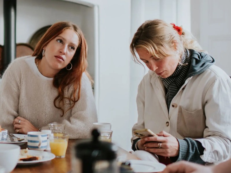 Teenagertochter sitzt genervt neben ihrer Mutter am Fr&uuml;hst&uuml;ckstisch.