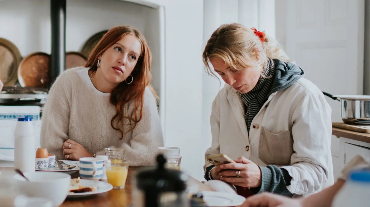 Teenagertochter sitzt genervt neben ihrer Mutter am Frühstückstisch.