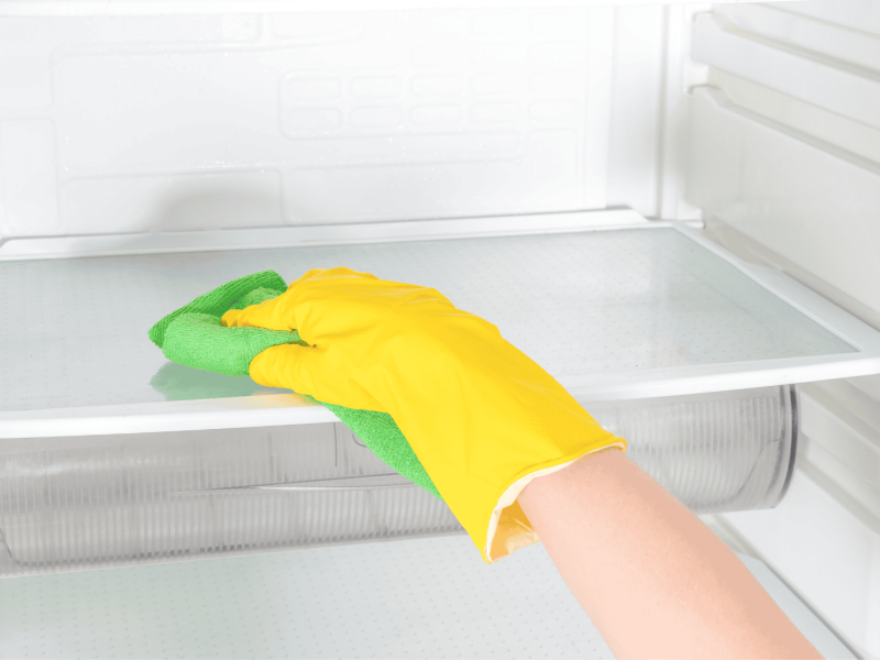 Person mit gelbem Reinigungshandschuh wischt durch K&uuml;hlschrank.