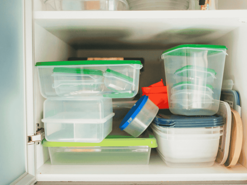 Voller Küchenschrank mit Plastikbehältern.