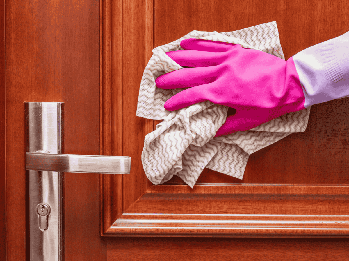 Person mit pinkem Putzhandschuhe wischt mit Lappen &uuml;ber Wohnungst&uuml;r.