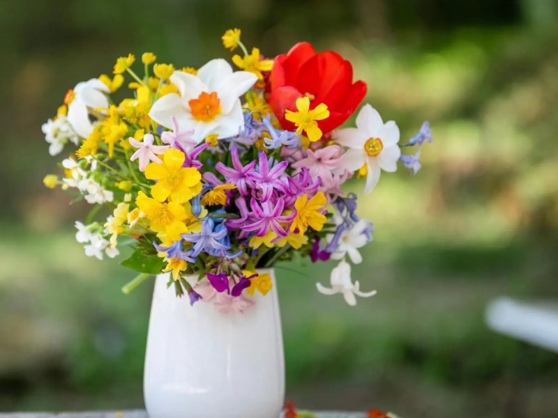 Verschiedene Wildblumen in einer weißen Vase stehen draußen auf dem Tisch.