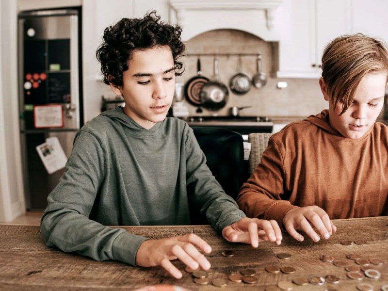 Zwei Jungs im Teenageralter zählen Geldmünzen auf dem Küchentisch.