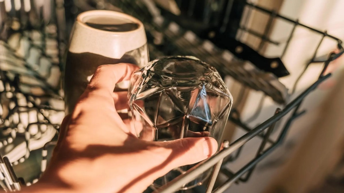 Frau räumt ein Glas in die Spülmaschine.