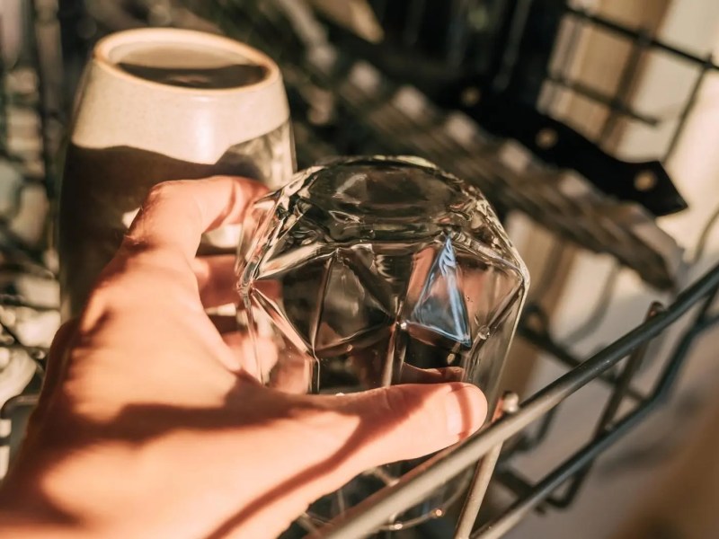 Frau räumt ein Glas in die Spülmaschine.