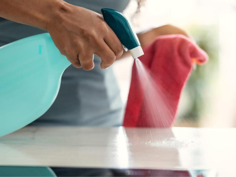 Frau spr&uuml;ht Wasser auf eine K&uuml;chenoberfl&auml;che und h&auml;lt einen Lappen in der Hand.