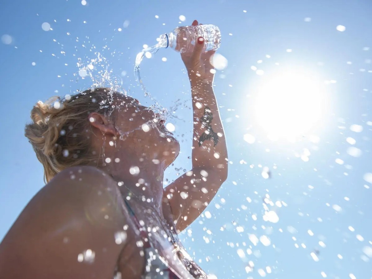 Frau gießt sich an einem sonnigen Tag Wasser über den Kopf.