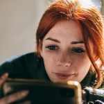 Frau mit roten Haaren und einem Smartphone in der Hand