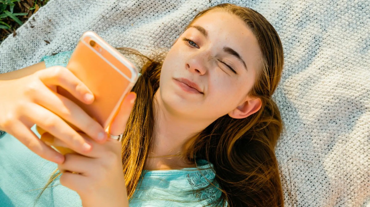 Teenie-Mädchen liegt auf einer Decke und scrollt am Handy.