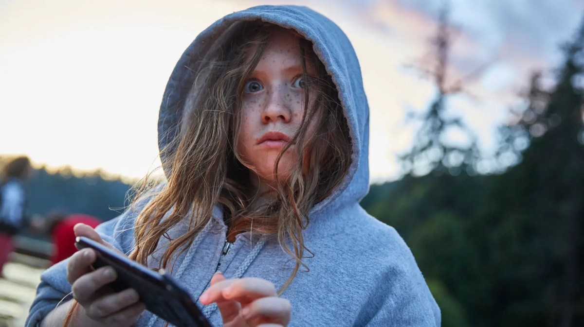 Mädchen im Hoodie am Telefon schaut erschrocken in die Kamera.