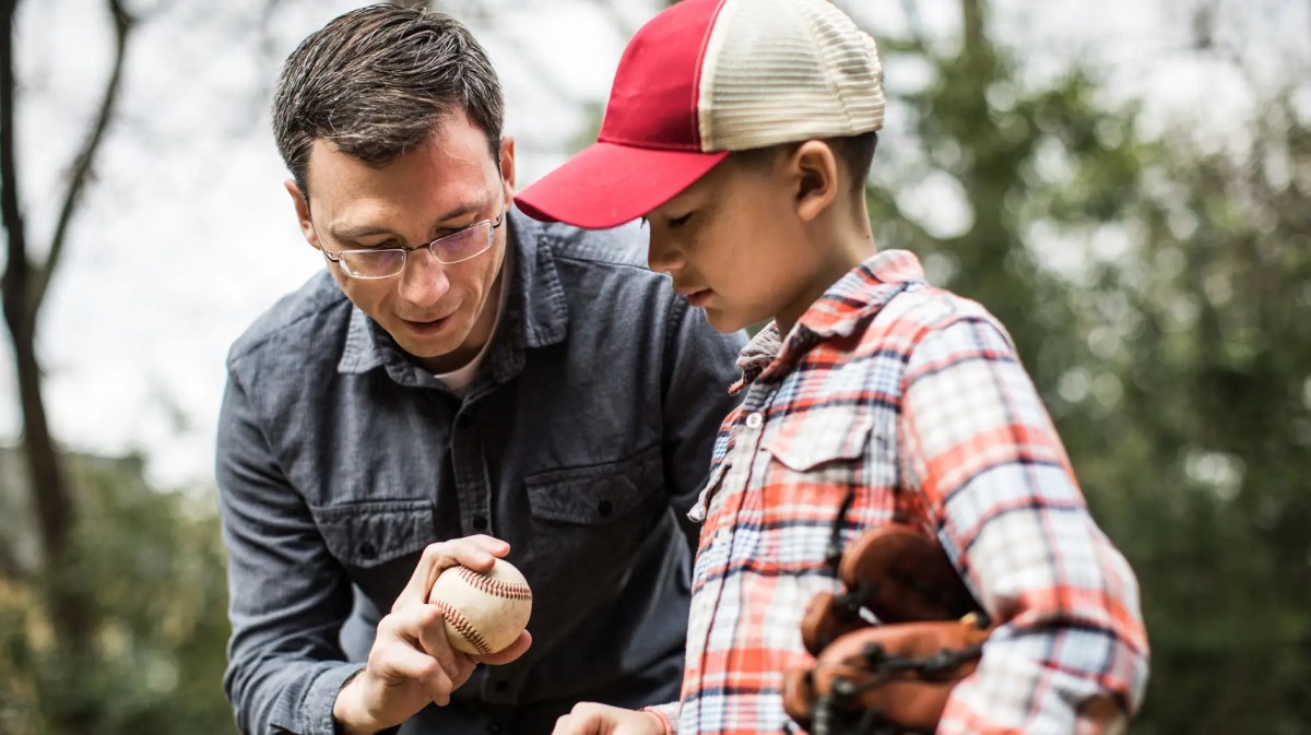 Vater erklärt Sohn, wie er den Baseball richtig wirft.