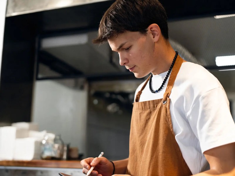 Teenager mit Schürze und Tablet in einem Restaurant.